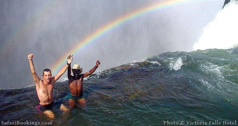 Tourists in Devil's Pool, Victoria Falls with rainbow