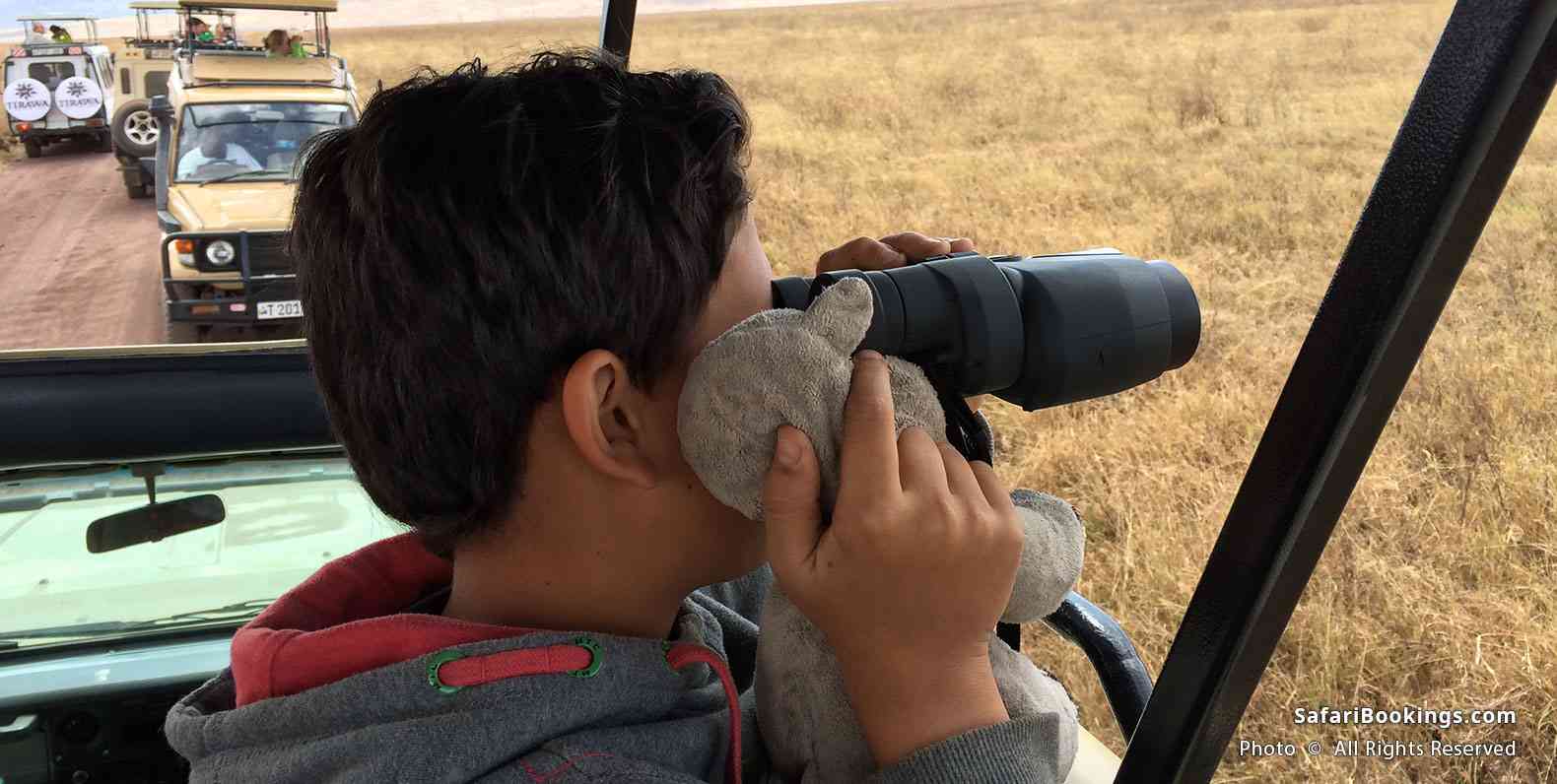 Kid looking through binoculars with stuffed rhino at Ngorongoro Crater