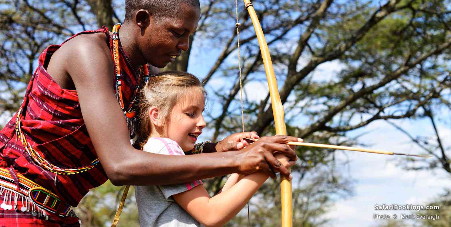 Girl shooting bow and arrow with Masai warrior