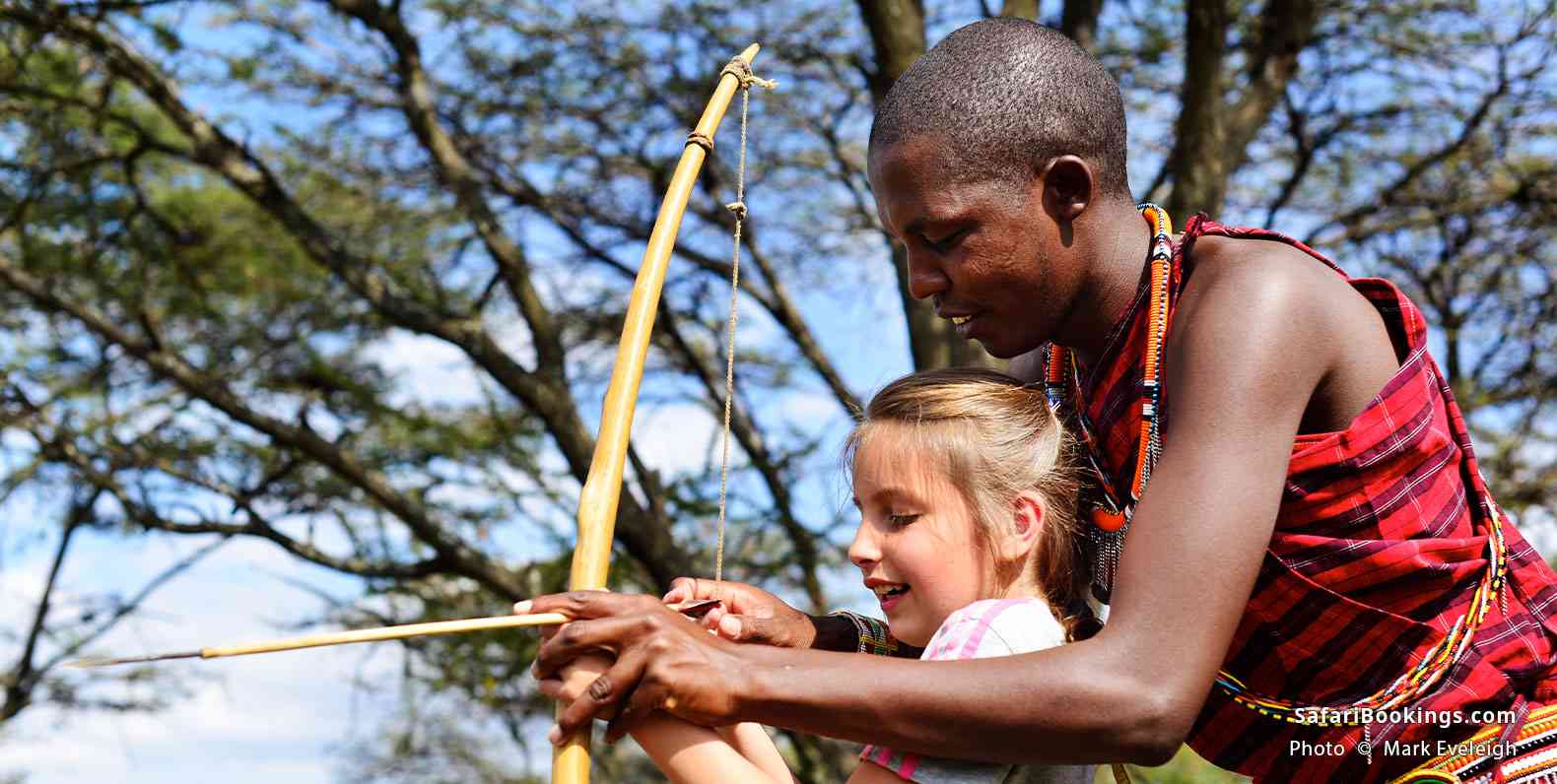 Maasai teaching girl to shoot a bow and arrow