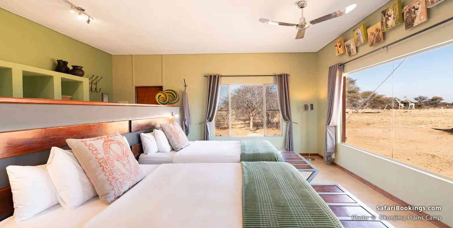 Luxury room at Okonjima Plains Camp and giraffes walking in the distance, seen through a broad window