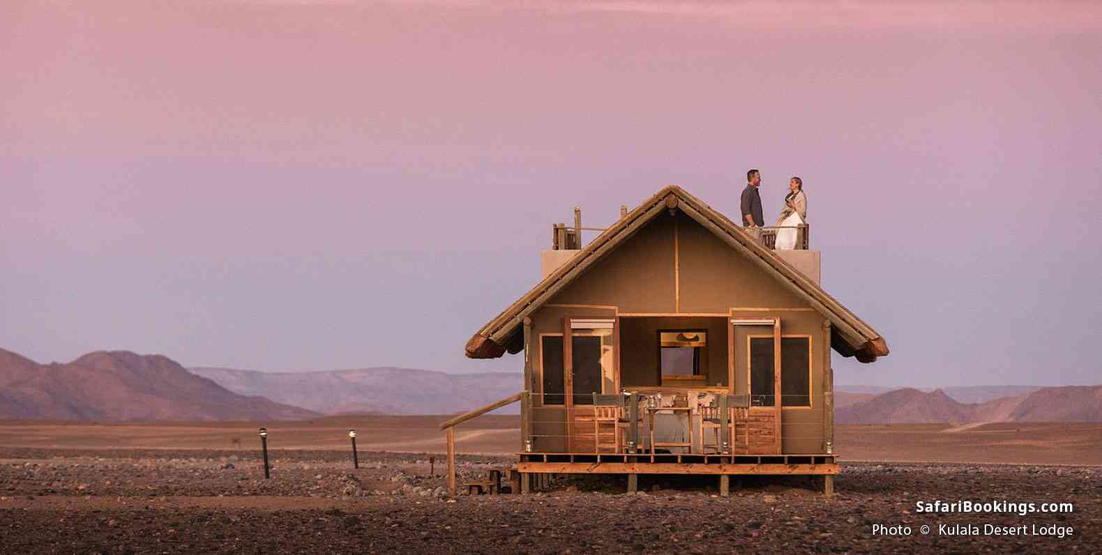 Couple standing on a rooftop terrace of a Kulala Desert Lodge chalet and enjoying the dusk