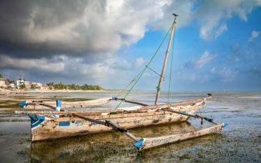 Traditional wooden dhow with outriggers on the beach at low tide in Jambiani